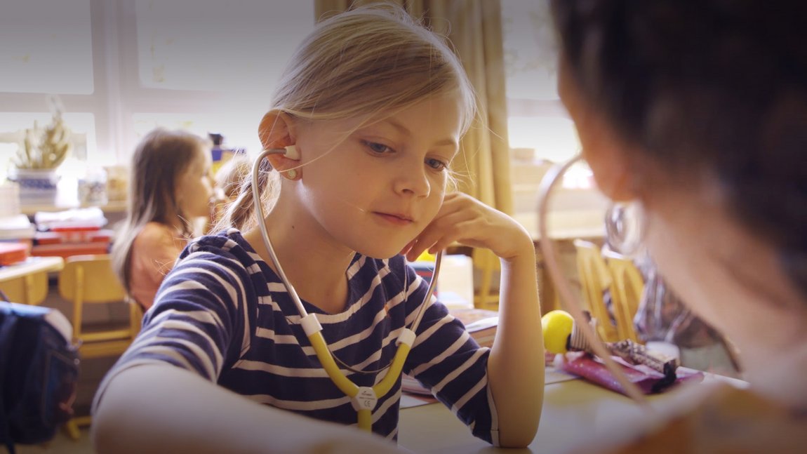 Mädchen sitzt im Klassenzimmer und hat ein Stethoskop in den Ohren