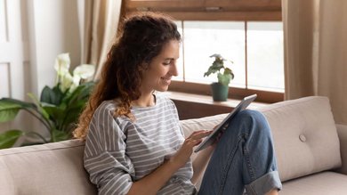 Eine junge Mutter sitzt auf der Couch und liest auf ihrem Tablet.